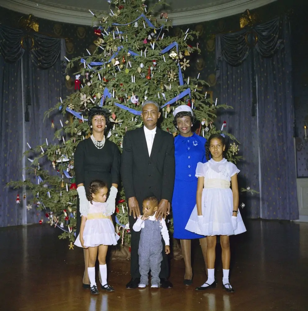 A White House staff member and his family stand before the 1961 White House Christmas tree during a reception held by the Kennedys. 