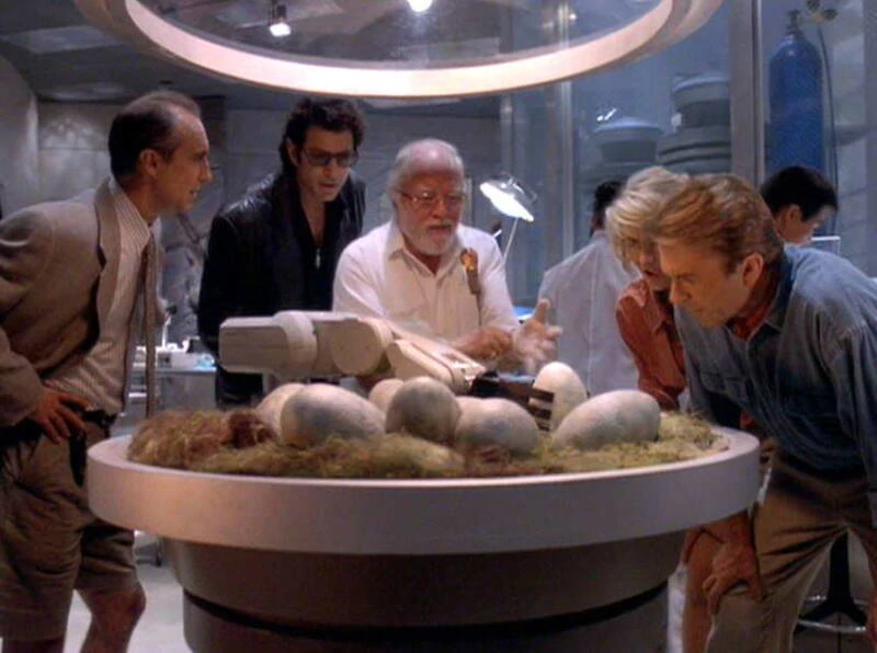 Jurassic Park characters gathered around the egg incubator. 